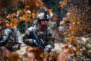 Soldier in camouflage gear in a forest during training.
