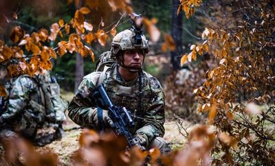 Soldier in camouflage gear in a forest during training.