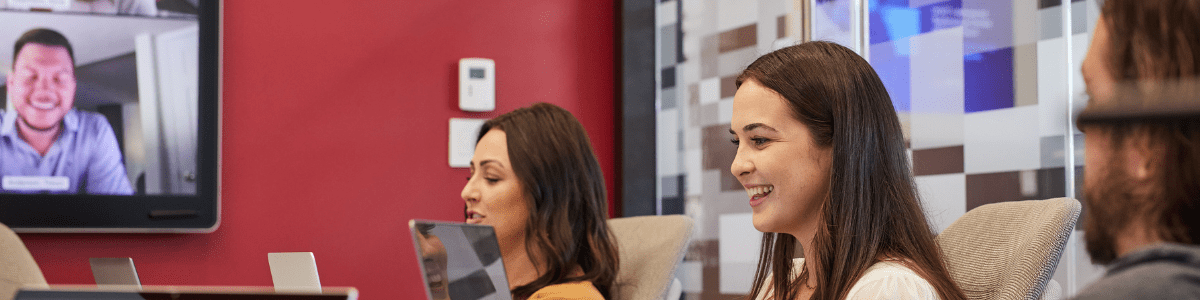 An intern and other people working on laptops in a conference room, participating in a video call.