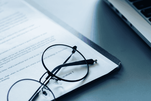 A pair of glasses resting on a printed contract sitting on a desk next to an open laptop
